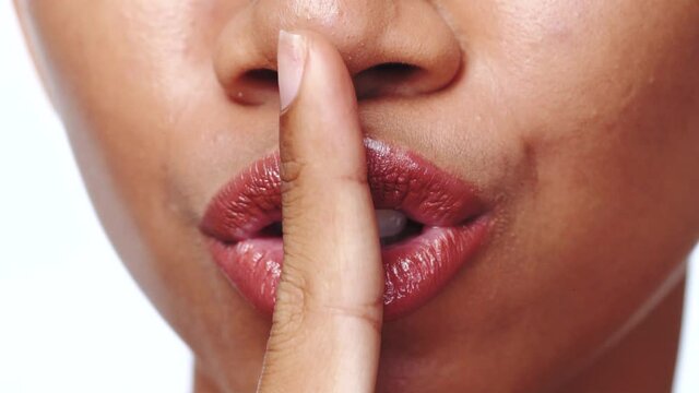 Cropped portrait of woman over white background extreme closeup. Closeup woman giving a shushing gesture raising her finger to her lips as she asks for silence - video in slow motion