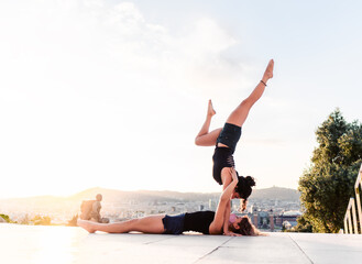 Two beautiful women doing acroyoga in the city. Harmony and relaxation with urban view