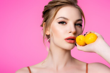 elegant beautiful blonde woman holding apricots isolated on pink