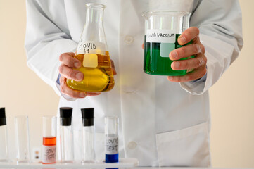 Covid-19 Reseracher in a lab coat holds a filled flask and beaker. Test tubes in the foreground.