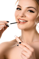 smiling naked beautiful blonde woman with makeup and black nails applying beige lip gloss isolated on white