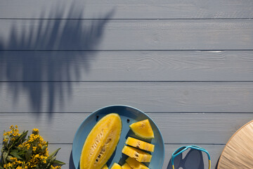 Summer flat lay in yellow and blue colors with yellow watermelon, sunglasses, flower bouquet and cap visor on wooden background. Copy space available