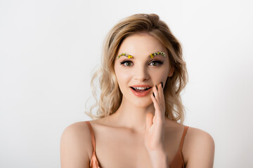 Naklejka premium surprised beautiful blonde woman with wildflowers on eyebrows isolated on white
