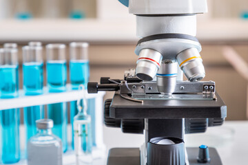 Close-up of microscope examining slide of sample with test tubes in background. Concept for science and technology research in laboratory.