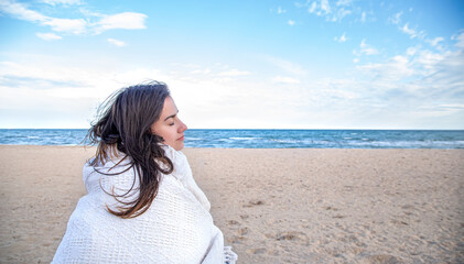 Obraz premium A young woman by the sea is covered with a blanket