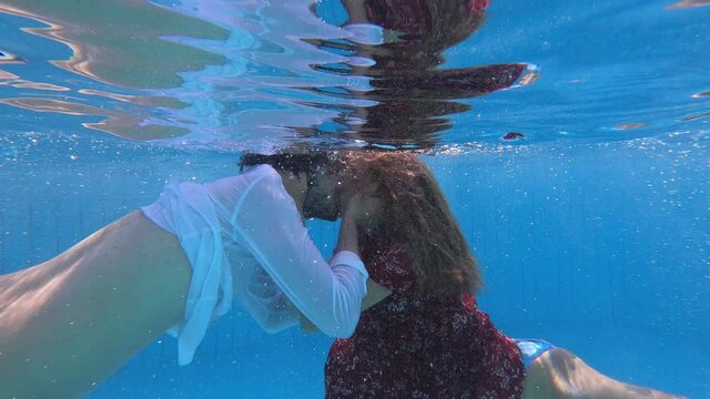 young couple kissing underwater in the pool and rising to the surface