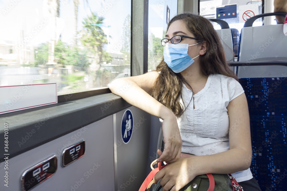 Canvas Prints Young Caucasian woman sitting in the bus with a medical face mask - the concept of new normal