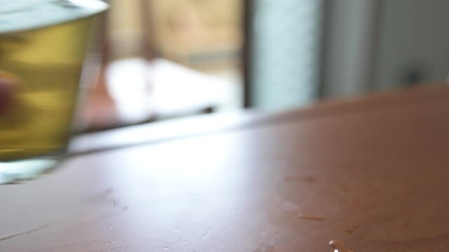Close-up image of a cold herbal tea: the glass is covered with condensation. The sachet is infused in the glass. A Caucasian man's hand grabs the glass: after drinking it he puts it back.
