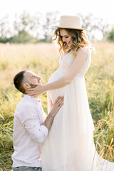 Happy pregnant couple in wild summer field outdoors. Portrait of a young pregnant couple enjoying their walk in field. Outdoors family lifestyle, happy family, motherhood concept