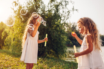 Little girls sisters blowing soap bubbles in spring park. Kids having fun playing games outdoors....
