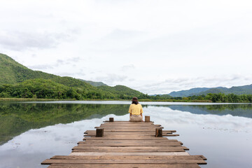 Woman setting on wooden bridge or small pier enjoy and look in the lake and mountain.