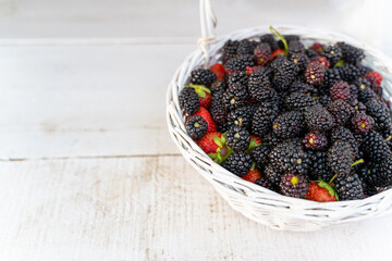 blackberries and strawberries in a white basket on a wooden rustic table background. Beautiful summer harvest time aroma horizontal composition. Poster template banner empty copy space. Farmer picking