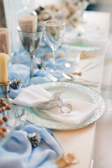Fototapeta na wymiar Festive table setting for Christmas and New Year in blue colors. Hummingbird figurine decorates plate.