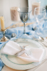 Fototapeta na wymiar Festive table setting for Christmas and New Year in blue colors. Hummingbird figurine decorates plate.
