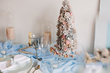 
Festive table setting for Christmas and New Year in blue colors, with artificial Christmas tree, candles and cutlery. Soft focus.