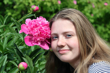 Naklejka premium girl with freckles poses in the garden with a peony flower