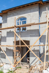 facade of cottage under construction covered with plaster with new windows inserted