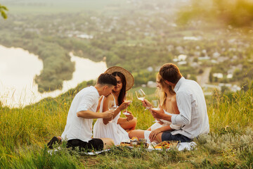 Smiling young people enjoying company, nature and scenic view. Group of friends making picnic in the nature. Happy people having fun on a picnic in the countryside.