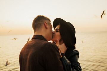 Close up portrait of a beautiful stylish young couple in love standing and kissing on the beach at sunset. Copy space.