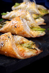 Green asparagus and cheese puff pastry folded as envelope on the black wooden board