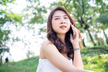 Cheerful young woman talking smartphone in city green park