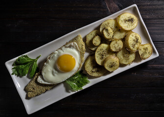 Hake fillet with fried egg and natural potatoes on black wooden boards