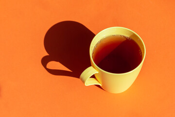 hot tea in a yellow plastic cup against orange background. hard light and deep shadows picture with space for text 
