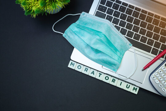 Surgical face mask on a laptop with block letters on moratorium on black table 