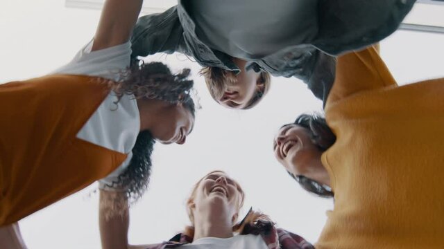 Group of women standing in a huddle and jumping outdoors. Low angle view of female friends forming a huddle and having fun.
