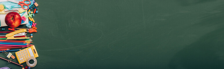 top view of ripe apple and school stationery on green chalkboard, horizontal image