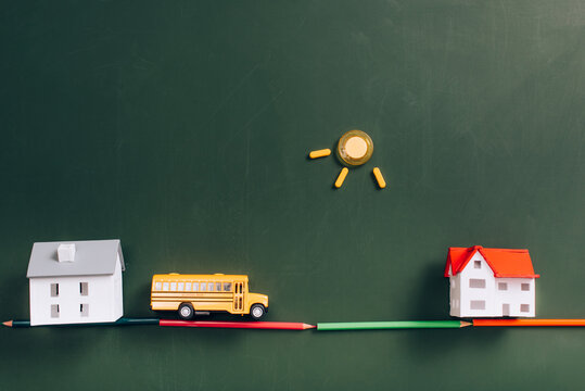 Top View Of Toy School Bus On Road Made Of Color Pencils, House Models And Sun Made Of Magnets On Green Chalkboard