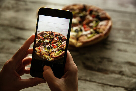 Female hands holding a smartphone and taking photo of a delivered pizza.