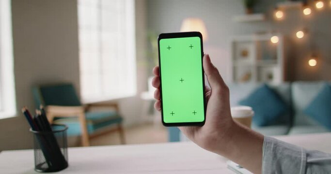 Close up shot of hand of guy holding a smartphone in cozy living room. A green screen mock up chroma key template 4k footage