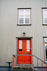 An orange door with glass and curtains in a building with white walls, steps with a handrail and plastic windows.