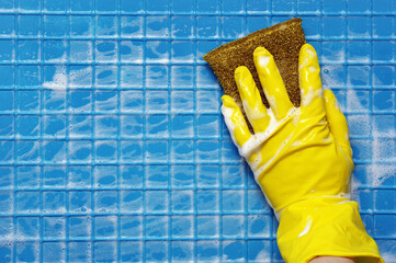 Hand in yellow glove with golden sponge on blue foam cleaning surface