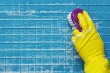 Hand in yellow glove with brush on a blue surface of white foam