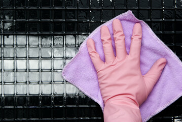A hand in a pink glove with a purple rag cleans a white surface with cells from black mud