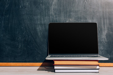 laptop with with blank screen on stack of textbooks near black chalkboard