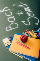 Selective focus of school supplies and fresh apple near back to school text on green chalkboard