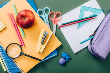 Top view of whole apple and notebooks near school stationery on green chalkboard © LIGHTFIELD STUDIOS