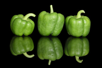 Three green bell peppers on a contrasting black background with bright reflection in the glass