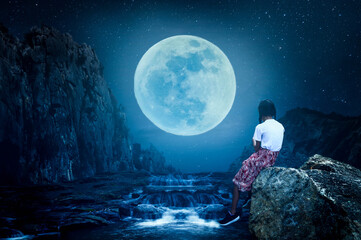 The little girl sat on a rock, watching the full moon on a lonely night.
