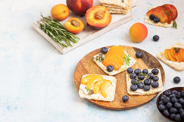 Mini rice cakes with blueberries, apricots, nectarine and cream cheese with honey for healthy breakfast. Light blue concrete background. Summer dieting sandwiches.