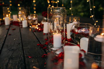 Romantic evening concept. White candles in glass vases and lights on the background on a wooden floor.