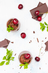 Homemade dark chocolate mousse garnish with sweet cherry and mint and pieces of chocolate on light...