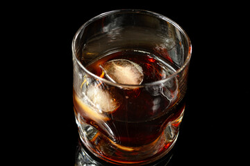 glass with whiskey and two ice cubes photographed in black background