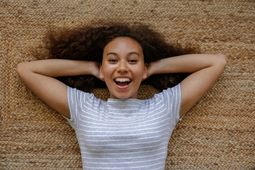 Top view portrait of young woman with dark skin and long curly hair lying on the floor. African...