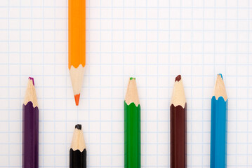 sharp orange pencil and blunt colored pencils on a writing-book leaf