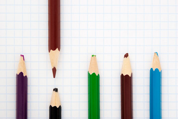 sharp  brown pencil and blunt colored pencils on a writing-book leaf