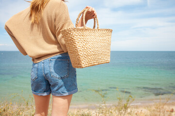 girl holding a summer straw bag on the background of the sea, woman showing beach bag